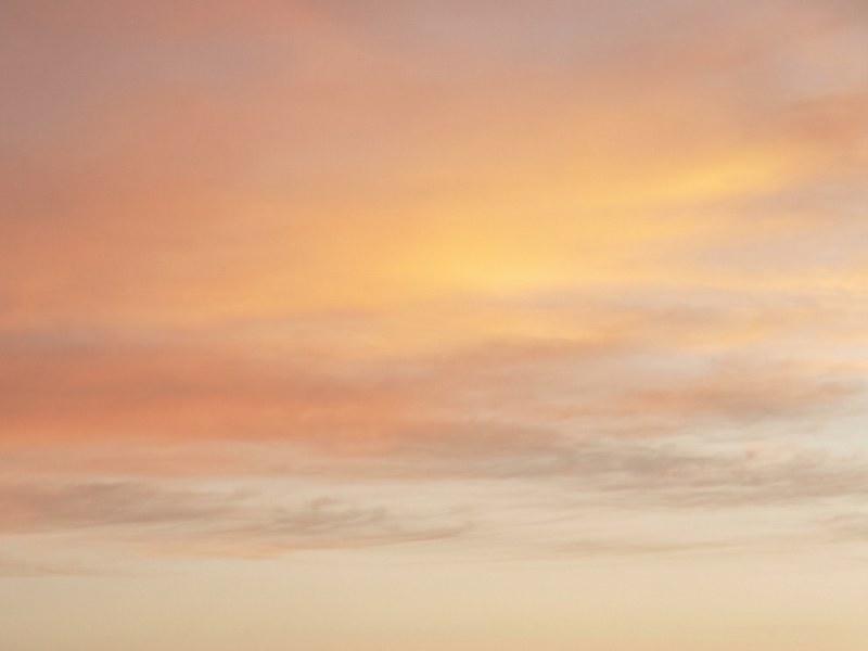 Céu de amanhecer em tons de pêssego, coral e creme, com bandas horizontais de nuvens claras junto ao horizonte.